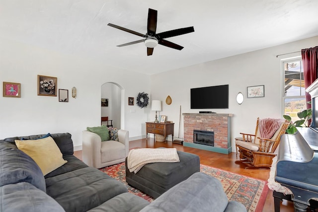 living area with arched walkways, ceiling fan, wood finished floors, and a fireplace