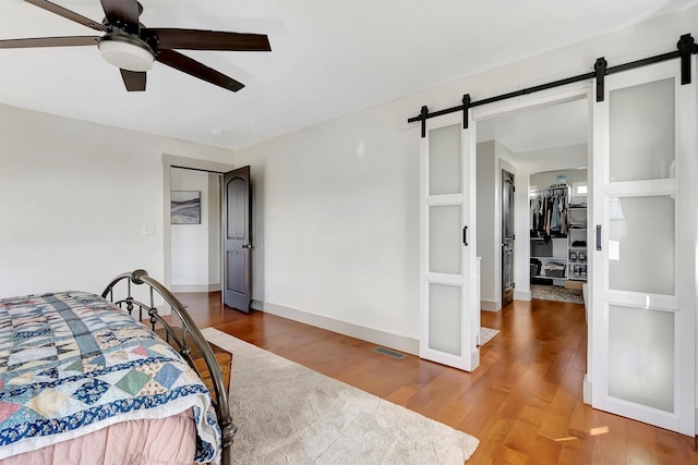 bedroom featuring wood finished floors, ceiling fan, a barn door, and visible vents