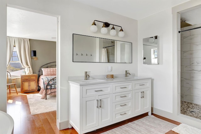 bathroom featuring a sink, double vanity, baseboards, wood finished floors, and tiled shower