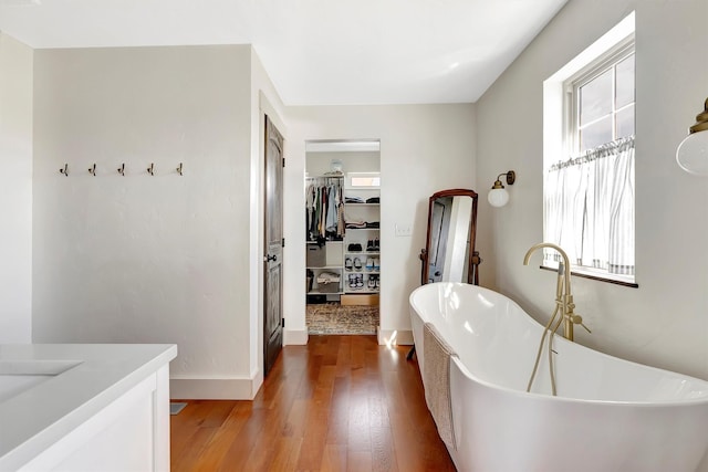 bathroom with a walk in closet, a freestanding bath, wood finished floors, baseboards, and vanity