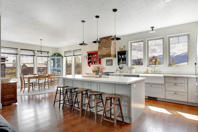 kitchen with wood finished floors, a kitchen bar, a center island, light countertops, and a sink