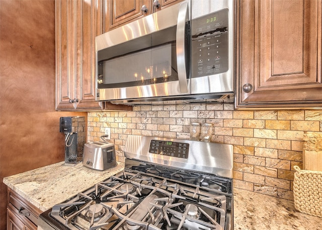 kitchen featuring brown cabinetry, appliances with stainless steel finishes, backsplash, and light stone counters