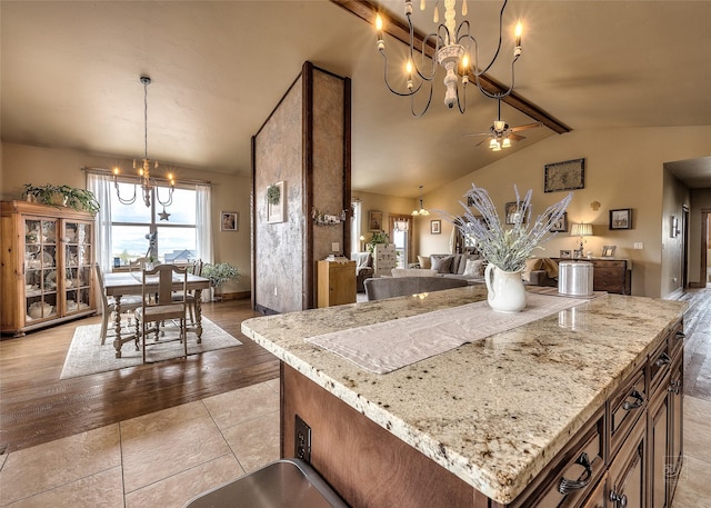 kitchen with lofted ceiling with beams, plenty of natural light, light stone counters, and ceiling fan with notable chandelier