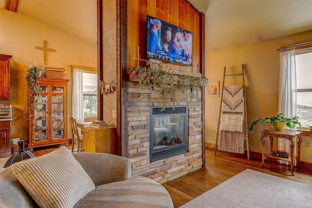 living room with vaulted ceiling with beams, a stone fireplace, and wood finished floors