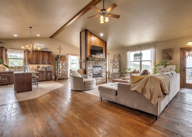 living area with light wood finished floors, a stone fireplace, ceiling fan with notable chandelier, recessed lighting, and vaulted ceiling with beams