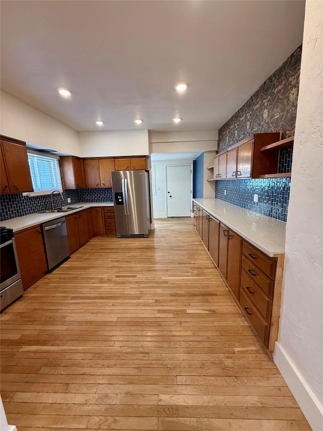 kitchen with open shelves, tasteful backsplash, a sink, light wood-style flooring, and appliances with stainless steel finishes