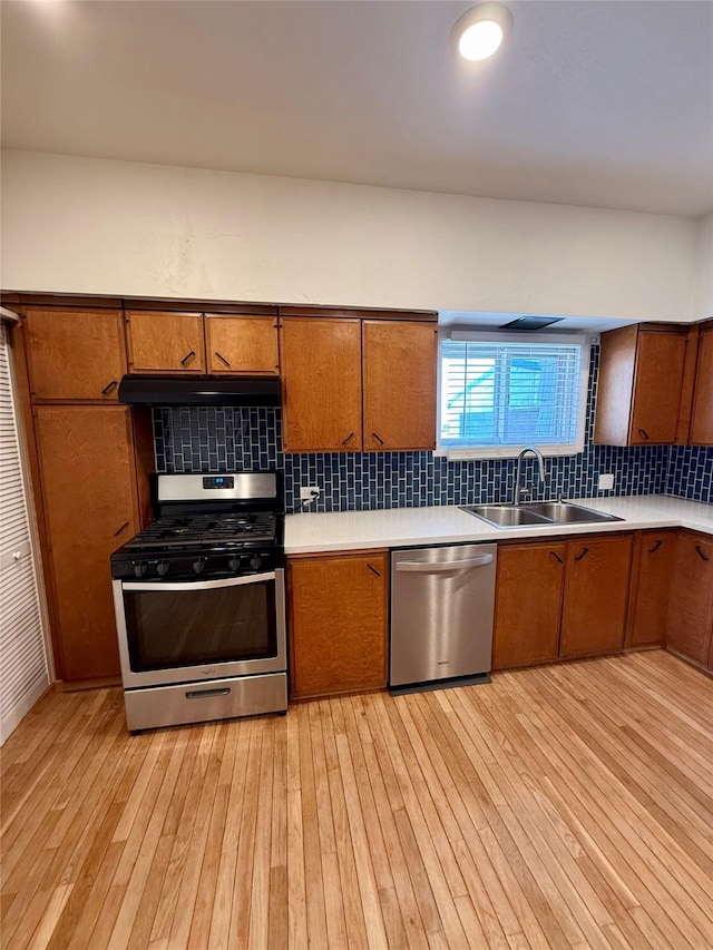 kitchen with a sink, appliances with stainless steel finishes, under cabinet range hood, and brown cabinets