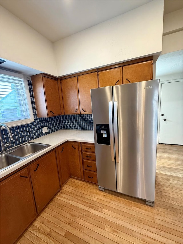 kitchen featuring a sink, brown cabinets, stainless steel refrigerator with ice dispenser, and light wood-style flooring