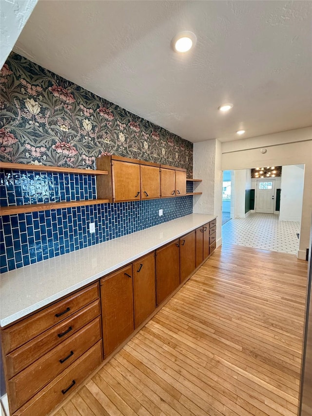 kitchen featuring brown cabinets, open shelves, light countertops, light wood-style flooring, and backsplash