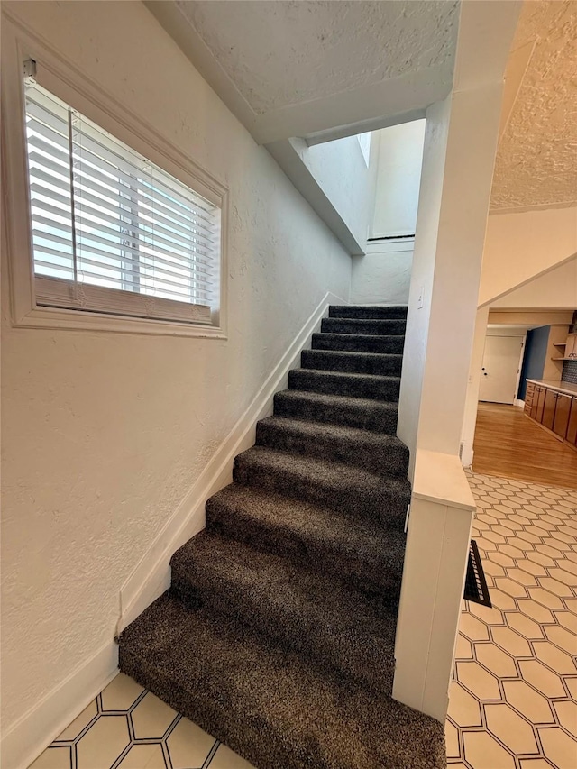 staircase featuring a textured ceiling and a textured wall