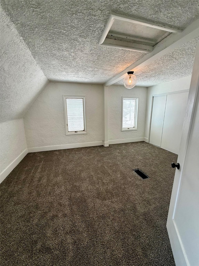 additional living space featuring a textured ceiling, visible vents, baseboards, and dark colored carpet
