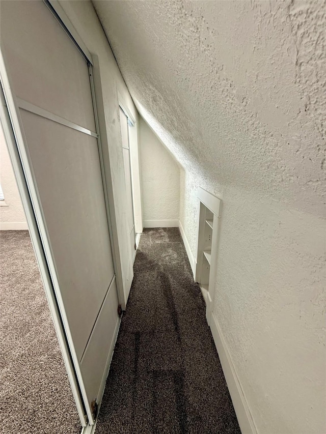 corridor with a textured ceiling, baseboards, lofted ceiling, a textured wall, and carpet flooring