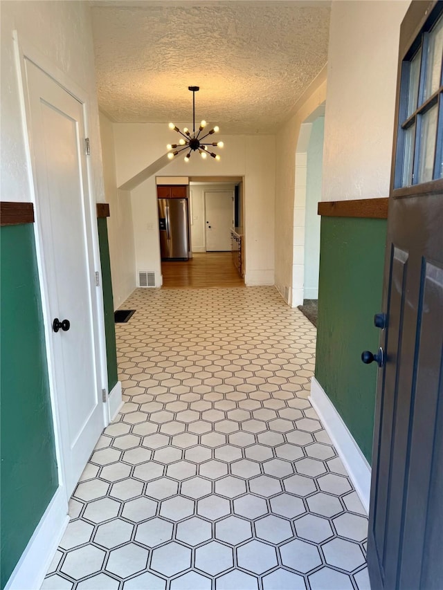 hallway featuring visible vents, baseboards, light floors, a textured ceiling, and a chandelier