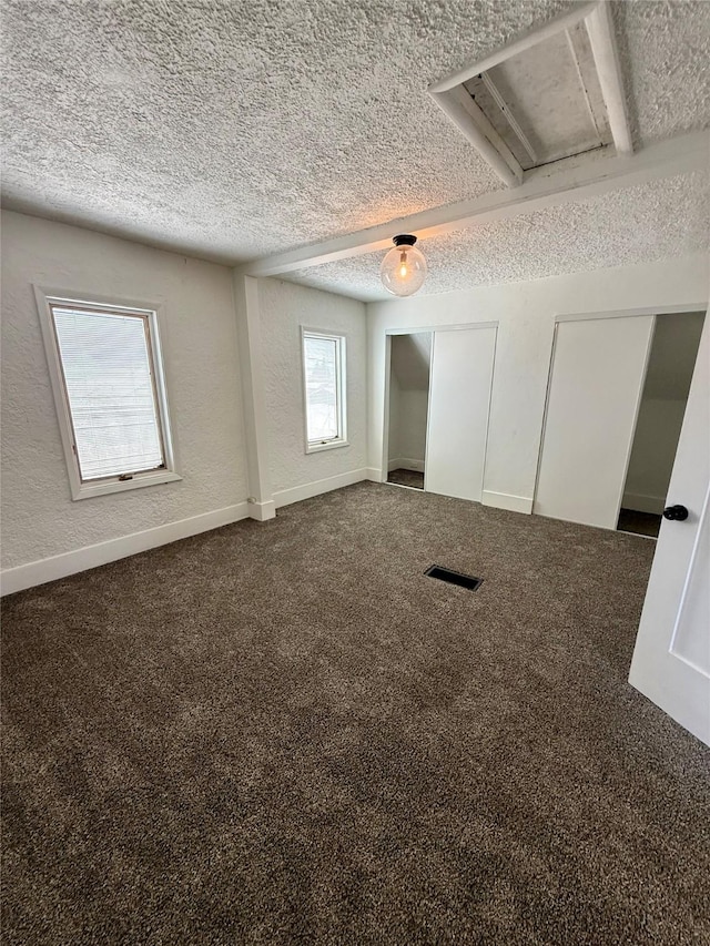 empty room with a textured wall, dark colored carpet, a textured ceiling, and visible vents