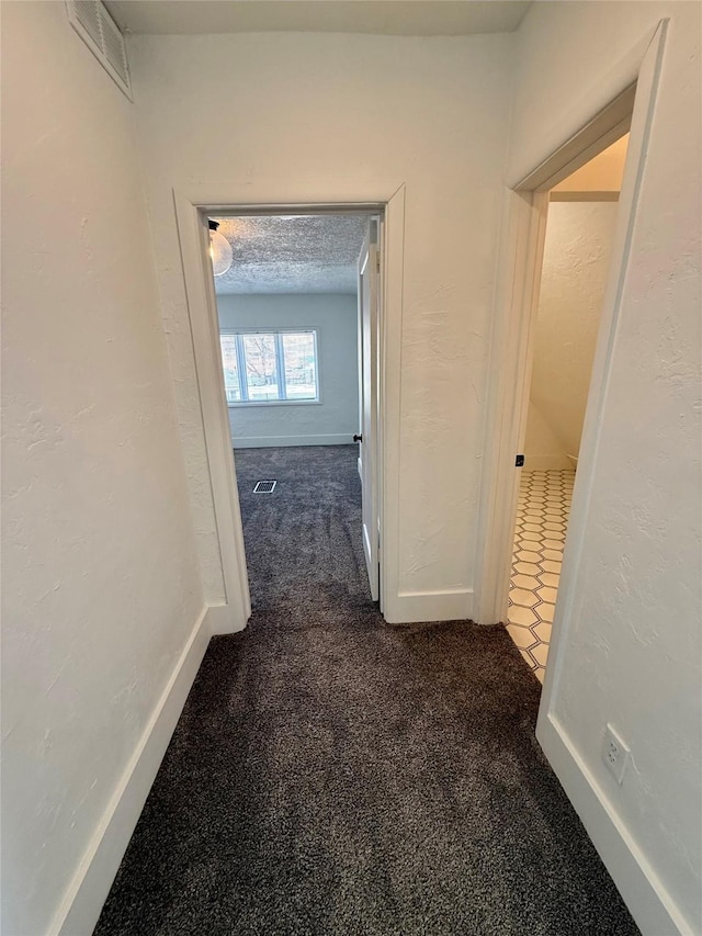 hall featuring baseboards, visible vents, and dark colored carpet