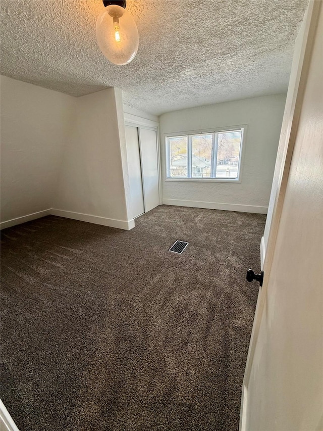empty room featuring a textured ceiling, baseboards, visible vents, and dark colored carpet