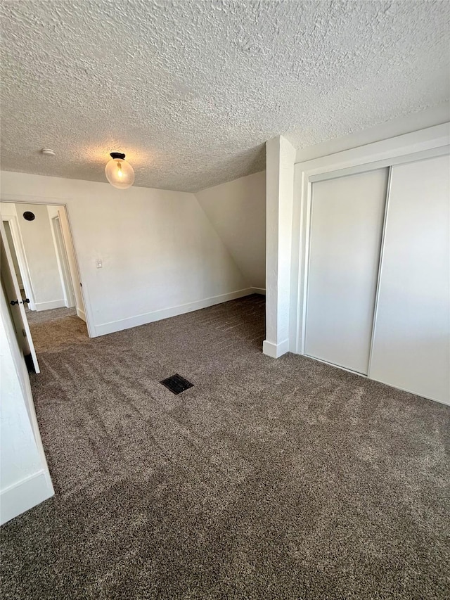 interior space featuring a textured ceiling, visible vents, carpet floors, baseboards, and a closet