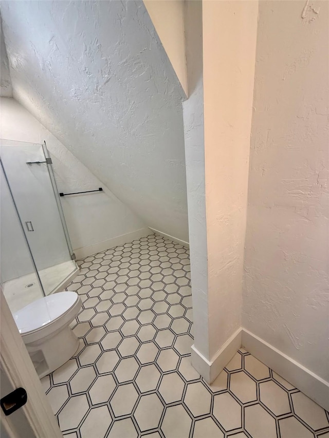 full bath with a textured wall, toilet, baseboards, a shower stall, and vaulted ceiling
