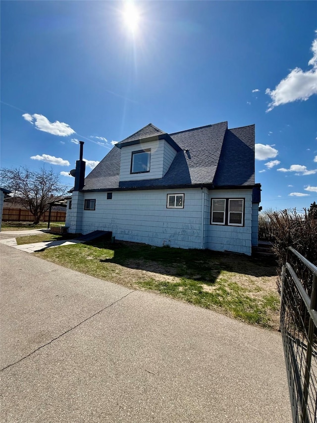 view of side of property with fence and roof with shingles