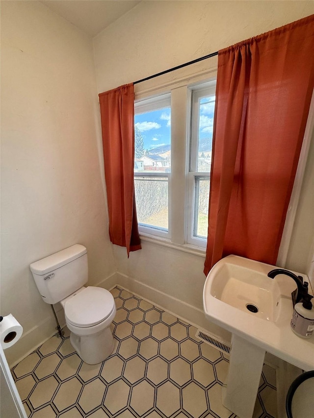 bathroom with a sink, baseboards, toilet, and visible vents