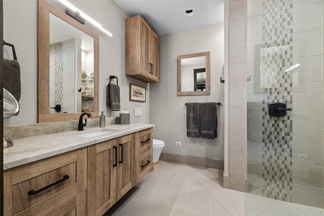 bathroom with tile patterned flooring, vanity, toilet, baseboards, and a tile shower