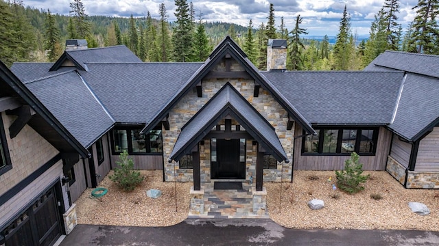 view of front of home featuring a wooded view, a chimney, and stone siding