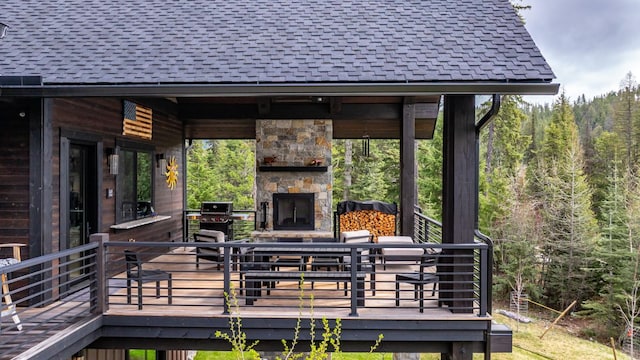wooden terrace featuring an outdoor stone fireplace and a wooded view