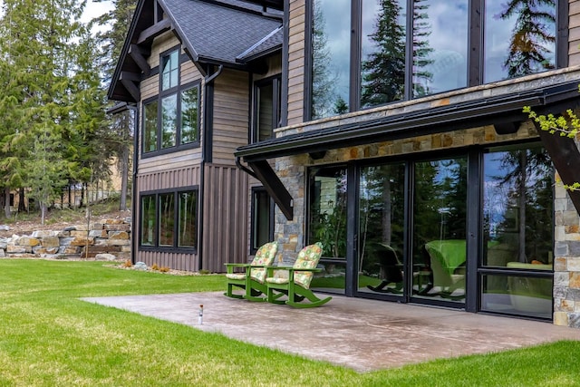 back of house featuring a lawn, a patio area, and stone siding