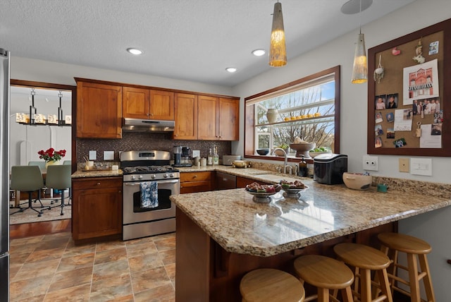 128 River View Dr, Kalispell, MT 59901 - kitchen featuring stainless steel range with gas cooktop, under cabinet range hood, a peninsula, brown cabinets, and backsplash