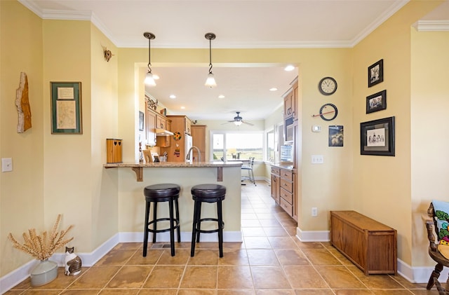 kitchen with brown cabinets, a kitchen breakfast bar, a peninsula, a ceiling fan, and ornamental molding
