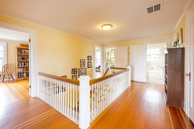 hall with crown molding, hardwood / wood-style flooring, an upstairs landing, and visible vents