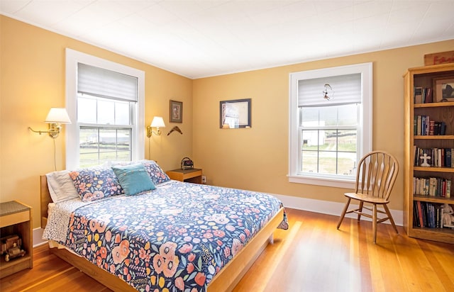 bedroom with baseboards, wood finished floors, and multiple windows