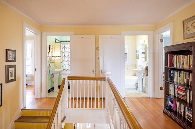 corridor with a sink, an upstairs landing, ornamental molding, and wood finished floors