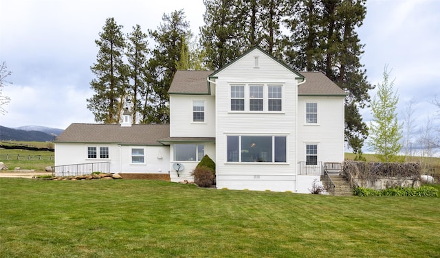 rear view of property featuring a lawn, stairway, fence, and a shingled roof