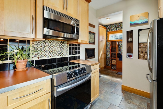 kitchen featuring stone tile flooring, decorative backsplash, light brown cabinets, baseboards, and stainless steel appliances