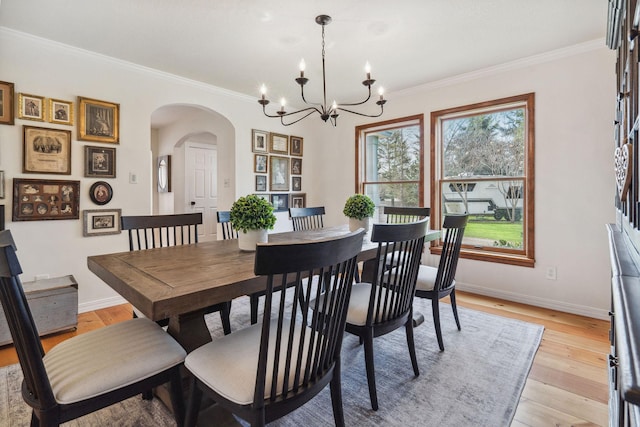 dining area with crown molding, baseboards, a chandelier, arched walkways, and light wood-style flooring