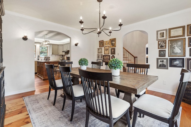 dining area featuring crown molding, arched walkways, light wood-type flooring, and a chandelier