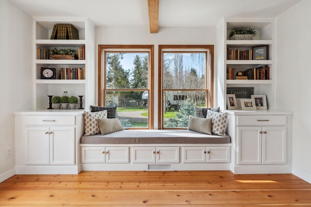living area with light wood-type flooring, beam ceiling, visible vents, and built in shelves