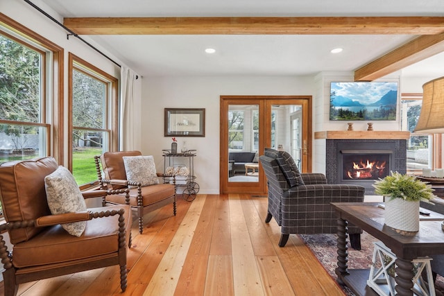 living area featuring a warm lit fireplace, beamed ceiling, a wealth of natural light, and light wood-style flooring