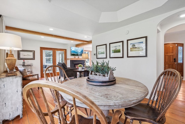 dining space featuring recessed lighting, arched walkways, light wood finished floors, and a warm lit fireplace