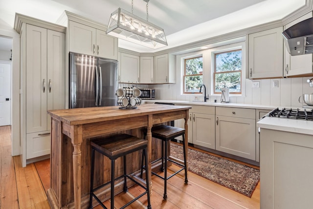 kitchen with exhaust hood, a sink, freestanding refrigerator, light wood-type flooring, and butcher block counters