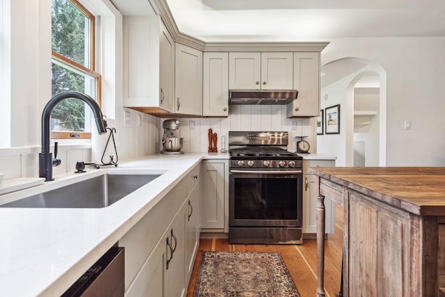 kitchen featuring decorative backsplash, gas range, a sink, light wood finished floors, and under cabinet range hood