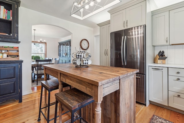 kitchen with freestanding refrigerator, arched walkways, a chandelier, and light wood-style flooring