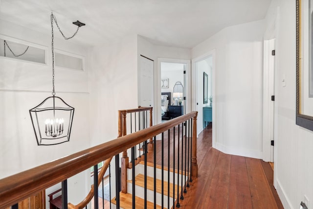 corridor with baseboards, an upstairs landing, dark wood finished floors, and a notable chandelier