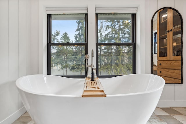 full bath featuring baseboards, a freestanding bath, and a decorative wall