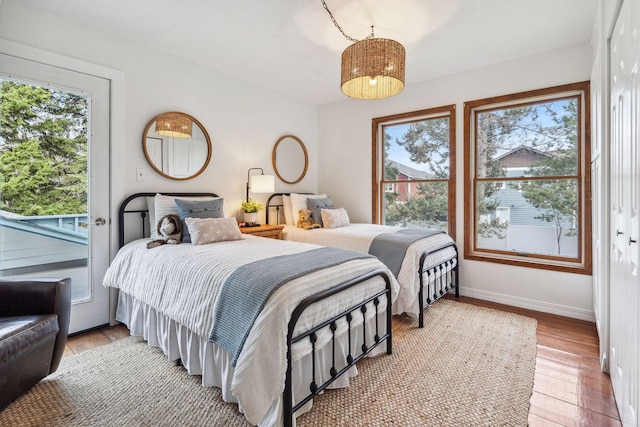 bedroom with access to outside, baseboards, wood finished floors, and multiple windows