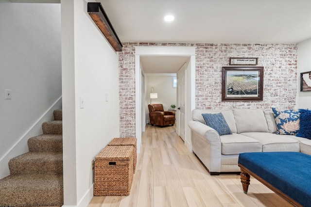 living area with light wood-style floors, stairs, and brick wall