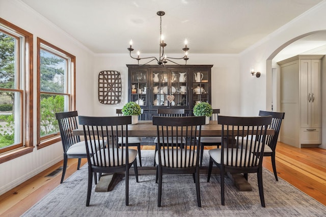 dining area featuring an inviting chandelier, arched walkways, light wood finished floors, and crown molding
