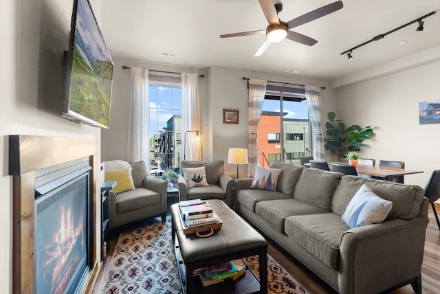 living area with track lighting, visible vents, wood finished floors, ceiling fan, and a lit fireplace