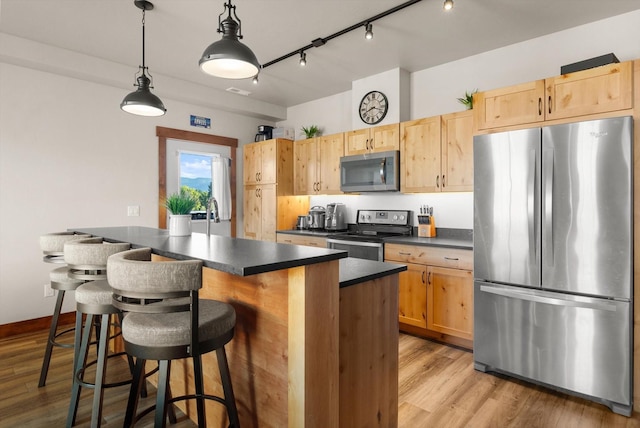 kitchen with light brown cabinetry, dark countertops, appliances with stainless steel finishes, a kitchen breakfast bar, and light wood-type flooring